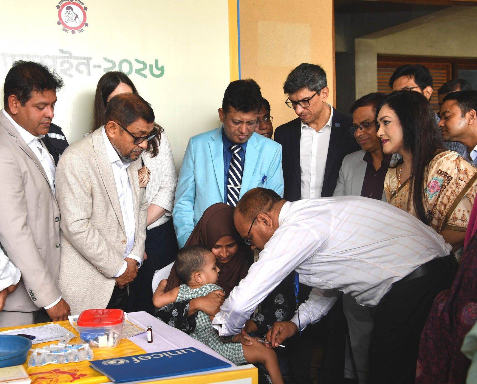 A health worker vaccinates a young child during a measles-rubella campaign session in Rupganj, Narayanganj, as officials watch.